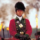 Ein Mann in roter Uniform mit hoher Mütze auf einem Pferd. Im Hintergrund brennende Fackeln.