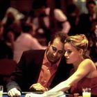 Zwei Personen sitzen an einem Tisch in einem belebten Raum, eine Frau zeigt dem Mann etwas.