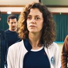 Eine Frau steht im Vordergrund einer Tennishalle, umgeben von drei Männern im Hintergrund.