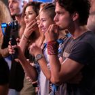 Junge Leute schauen konzentriert in eine Richtung, einer hält eine Kamera. Sie wirken fasziniert und nachdenklich.