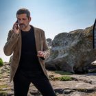 „La croix de Proëlla en mémoire de nos hommes perdus en mer...“ Ein Mann telefoniert in steiniger Landschaft.