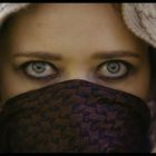 Keine erkennbaren Texte. Eine Person mit Kapuze und Bandana verdeckt den Mund, zeigt markante Augen.