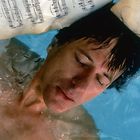 Handgeschriebene Musiknoten schweben auf Wasser. Ein Mann mit geschlossenen Augen ist teilweise untergetaucht.