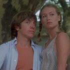 Es gibt keine sichtbaren Texte. Ein junger Mann und eine Frau stehen eng beieinander im Freien, in einem grünen, natürlichen Umfeld.