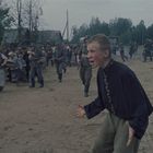 Eine aufgewühlte Szene mit Soldaten in Uniform, die Zivilisten treiben. Ein Junge vorne schreit verzweifelt. Bäume im Hintergrund.