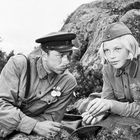 Ein Mann und eine Frau in Militäruniformen lehnen an Felsen und scheinen sich zu unterhalten.