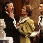 Eine Frau in Gelb spricht mit einem Mann, während eine andere Frau daneben steht. Eine Büste steht links. Vintage-Dekor.