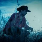 Zwei Personen in einer Wohnung halten abwehrend ihre Hände hoch. Blumenmuster an der Wand, dezente, warme Beleuchtung.