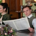 Ein Mann liest "Lloyd’s Weekly Newspaper". Neben ihm sitzt eine Frau in grüner Kleidung. Sie befinden sich in einem eleganten Raum.