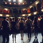 Ein Schauspielensemble steht auf der Bühne eines Theaters, blickt zum vollen, beleuchteten Zuschauerraum.