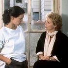 Zwei Frauen sitzen vor einem hellen Fenster und unterhalten sich. Eine trägt ein weißes Oberteil, die andere einen Schal.