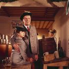 Eine gemütliche Szene in Trachten. Ein Mann und ein Kind stehen in traditioneller Kleidung, umgeben von Bierkrügen.