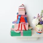 Mehrere bunte Geschenke mit blauen und roten Schleifen. Sticker in Form von Gebäck. Vase mit Blumen daneben.