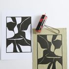 Schwarze abstrakte Formen auf weißem Papier, Druckrolle und Linolschnittblock nebeneinander liegend.