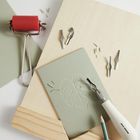 Ein Linolschnitt-Set mit einem geschnitzten Blattmotiv. Werkzeuge, eine Walze und ein Schnitzmesser sind zu sehen.