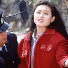 Die Uniformen der Männer zeigen „POLICE“ und eine Seriennummer. Eine Frau im roten Mantel wird von zwei Polizisten begleitet.