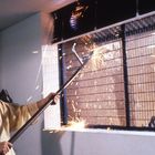 Text: "PLATINUM." Ein Mann in gelbem Pullover benutzt eine lange Metallstange, um Funken an einem Zaungitter zu erzeugen.