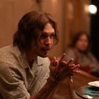 Es gibt keinen Text zu erwähnen. Eine Person mit langen Haaren sitzt an einem Tisch, konzentriert und nachdenklich.