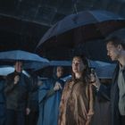 Eine Gruppe von Menschen steht im Regen unter blauen und schwarzen Regenschirmen. Zwei Personen sind im Vordergrund.