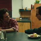 Zwei Männer sitzen am Tresen in einem Diner. Einer trägt ein kariertes Hemd, der andere eine Brille mit Pullover. Vor ihnen ein Stück Kuchen.