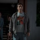 Eine Person trägt ein T-Shirt mit Comic-Panels. Die Umgebung wirkt dunkel, mit weiteren Personen im Hintergrund.