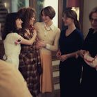 Eine Gruppe von Frauen in verschiedenen Outfits steht freundschaftlich beisammen und lächelt.