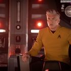 Mann in gelber Uniform sitzt in einem futuristischen Raum. Er wirkt konzentriert, umgeben von roten Lichtern und Bildschirmen.