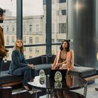 Vier Personen in eleganter Kleidung in einem modernen Büro mit großen Fenstern.