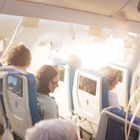 Ein heller Lichtblitz in einer Flugzeugkabine, Passagiere ducken sich, Sitzbildschirme eingeschaltet, lose Gegenstände fliegen umher.