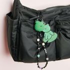 Großer schwarzer Rucksack mit grünem Kettenanhänger: ein lächelndes Tier. Die Kette hat bunte Perlen.