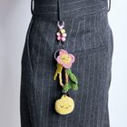 Kein Text sichtbar. Ein grauer Rock mit Nadelstreifen, daran hängt ein Schlüsselbund mit buntem Blumenanhänger und gelbem Gesicht.