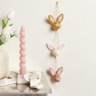 Hängende Filzhasen an einer Schnur, rosa gedrehte Kerze in weißem Halter, Vase mit weißen Tulpen.