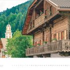 Kalender für September 2027. Eine rustikale Holzfassade mit Blumenkästen; im Hintergrund ein Kirchturm, umgeben von Tannen.