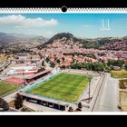 Kalenderblatt mit Zahl "11". Fußballstadion und Stadt im Hintergrund, umgeben von Hügeln und Natur.