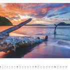 Kalenderblatt September 2027: Ein feuriger Sonnenuntergang am Strand mit einem Baumstamm im Vordergrund und Vulkan im Hintergrund.