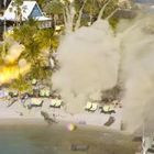 Es steht „Discover“ auf einem blauen Gebäude. Sandstrand mit Palmen, Liegen und einer Explosion. Menschen laufen panisch.