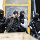 Männer in schwarzer Kleidung mit "Policia"-Abzeichen nehmen einen fest, in urbaner Umgebung.