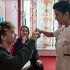 Eine Frau in weißer Arbeitskleidung führt einen Finger-Test mit einem sitzenden Jungen durch, während eine andere Frau zusieht.