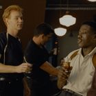 Ein Poster zeigt ein Guinness-Logo und den Text "good for you". Vier Personen stehen in einer gemütlichen Baratmosphäre.