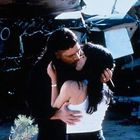 Ein Paar küsst sich innig vor dem Hintergrund eines Flugzeugwracks. Die Szene wirkt emotional und dramatisch.