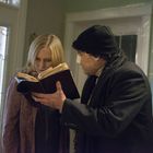 Es gibt keinen Text zu erwähnen. Zwei Personen betrachten gemeinsam ein geöffnetes Buch in einem Hausflur.