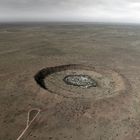 Es gibt keinen Text zu beachten. Eine weite, flache Landschaft mit einem kreisförmigen Krater in der Mitte. Wolken am Himmel.