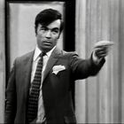 Ich kann keine Personen auf Bildern identifizieren. Ein Mann im Anzug zeigt mit ernster Miene in eine Richtung.