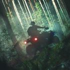 Ein ATV-Fahrer bewegt sich durch einen nebligen, dichten Wald; Scheinwerfer beleuchten die Bäume.