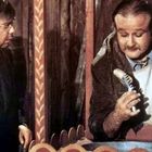 Zwei Männer, einer hält eine Wurst auf einer Gabel. Sie stehen vor einem bunten Hintergrund.