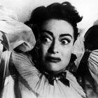 Keine erkennbaren Texte. Eine Frau mit weit aufgerissenen Augen wirkt erschrocken, in Kleidung mit bauschigen Ärmeln.