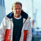 Eine Person trägt einen weißen Parka mit rotem Streifen und darunter einen dunkelgrünen Pullover.