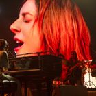 Eine Musikerin spielt am "Yamaha"-Klavier, große Nahaufnahme ihres singenden Gesichts im Hintergrund.