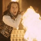 Ein Mann in einer eleganten Weste steht vor einer großen Flamme, mit weit geöffnetem Mund und begeistertem Ausdruck.