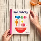 "The Bone Broth Book". Buntes Cover mit geometrischen Formen. Hände halten es. Nebenan ein Getränk auf gestreifter Decke.